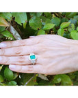 Hand wearing an 18K white gold engagement ring with a vibrant emerald and diamond halo.