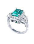 An elegant natural emerald engagement ring and diamond accents on a white background.