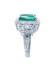A side profile of a natural emerald and a halo diamond engagement ring in 18k white gold.