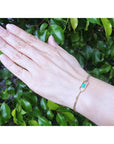 Hand wearing a 14K yellow gold bracelet with a square emerald-cut Colombian emerald.