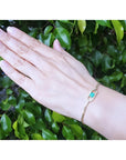 Hand wearing a 14K yellow gold bracelet with a square emerald-cut Colombian emerald.
