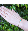 Hand wearing a 14K yellow gold bracelet with a square emerald-cut Colombian emerald.