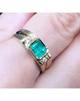 A 14k yellow gold men's ring with a bezel set emerald on a person's finger.