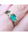 A 14k yellow gold men's ring with a bezel set emerald on a person's finger.