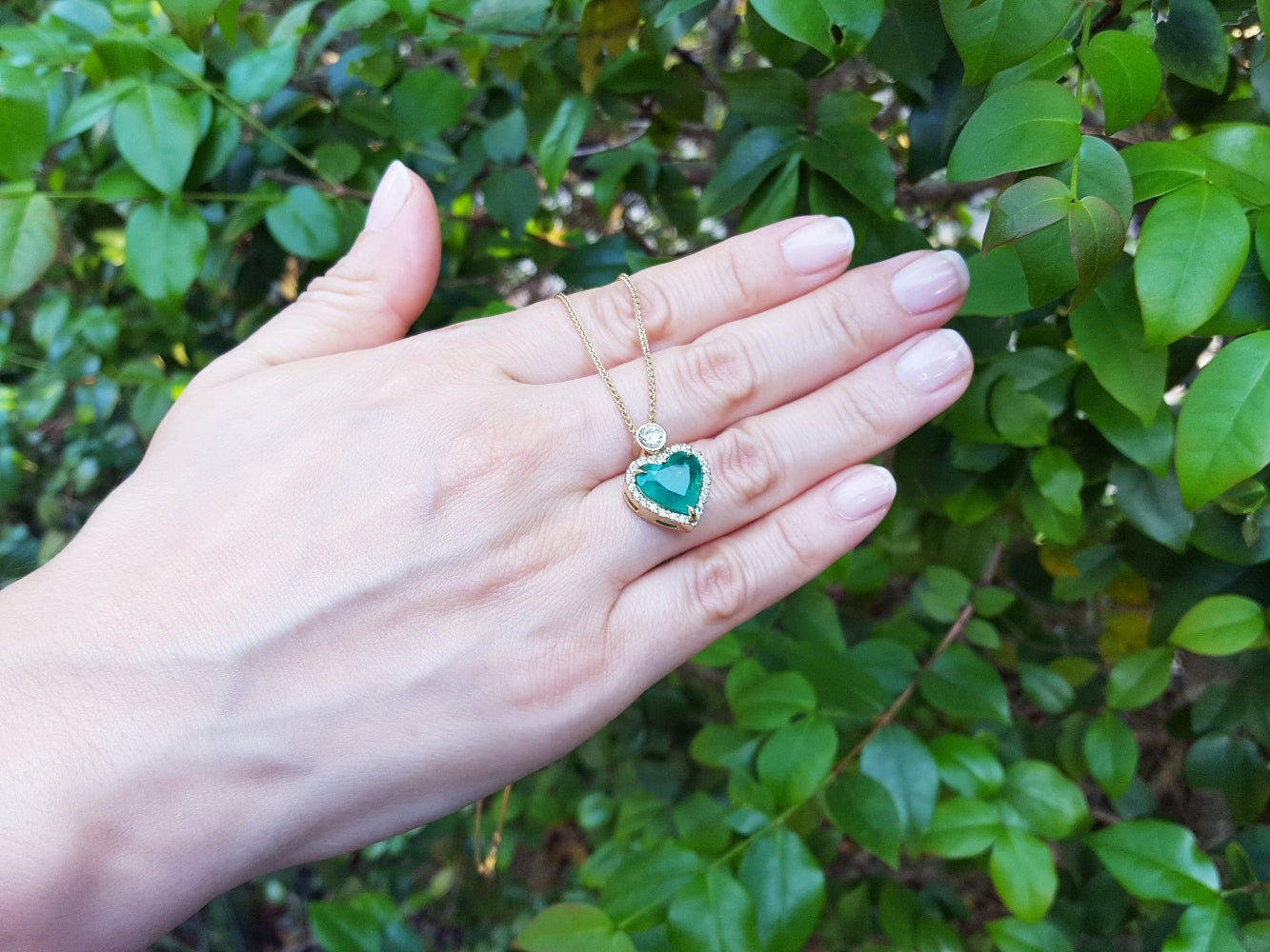 Hand holding a heart-shaped natural pendant necklace against a green leafy background.