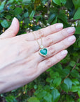 Hand holding a heart-shaped natural pendant necklace against a green leafy background.