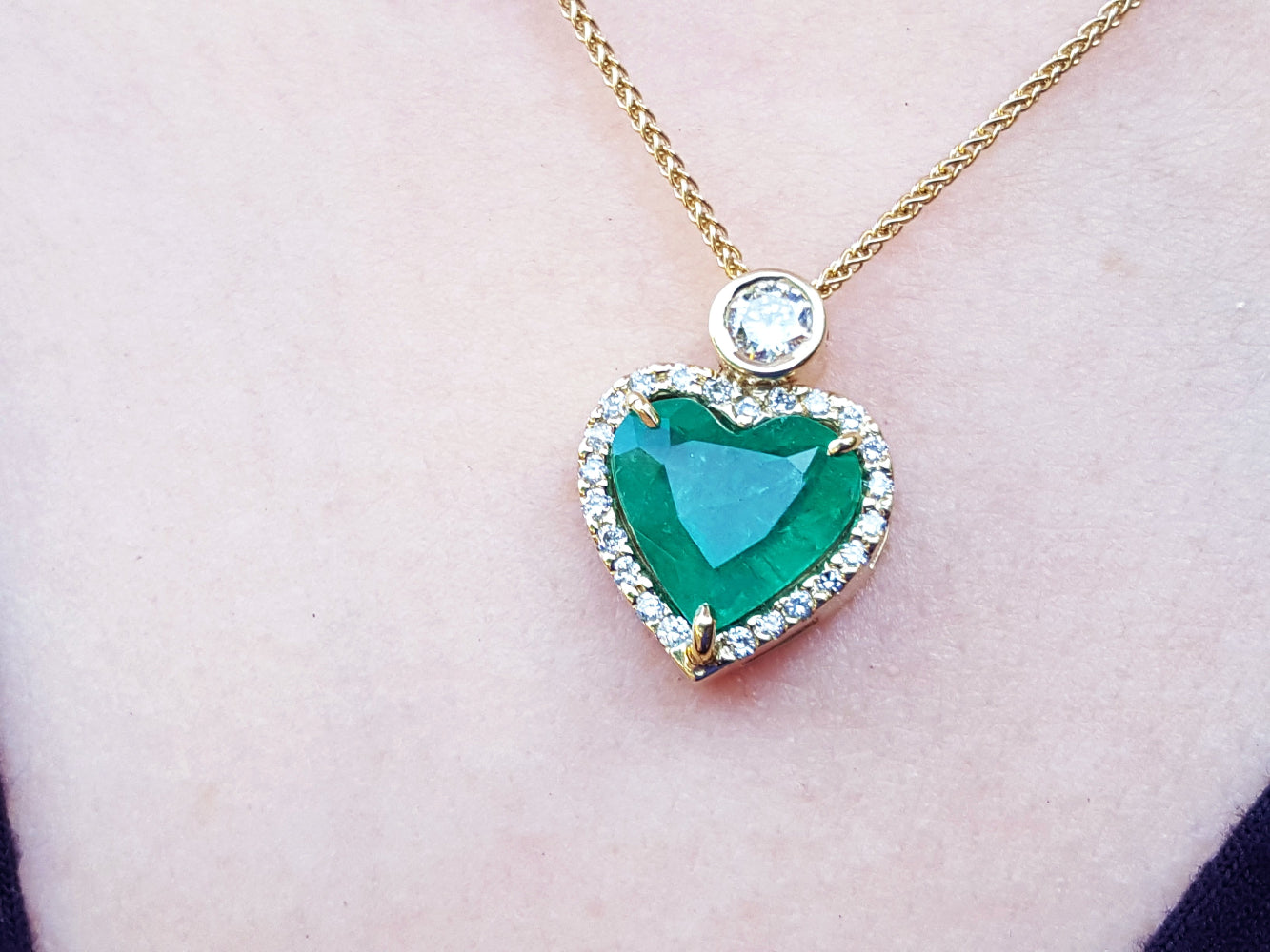 Heart-shaped emerald pendant on a gold chain against a skin background.