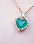 Heart-shaped emerald pendant on a gold chain against a skin background.