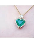 Heart-shaped emerald pendant with diamond halo and round diamond accent on an 18k gold chain.