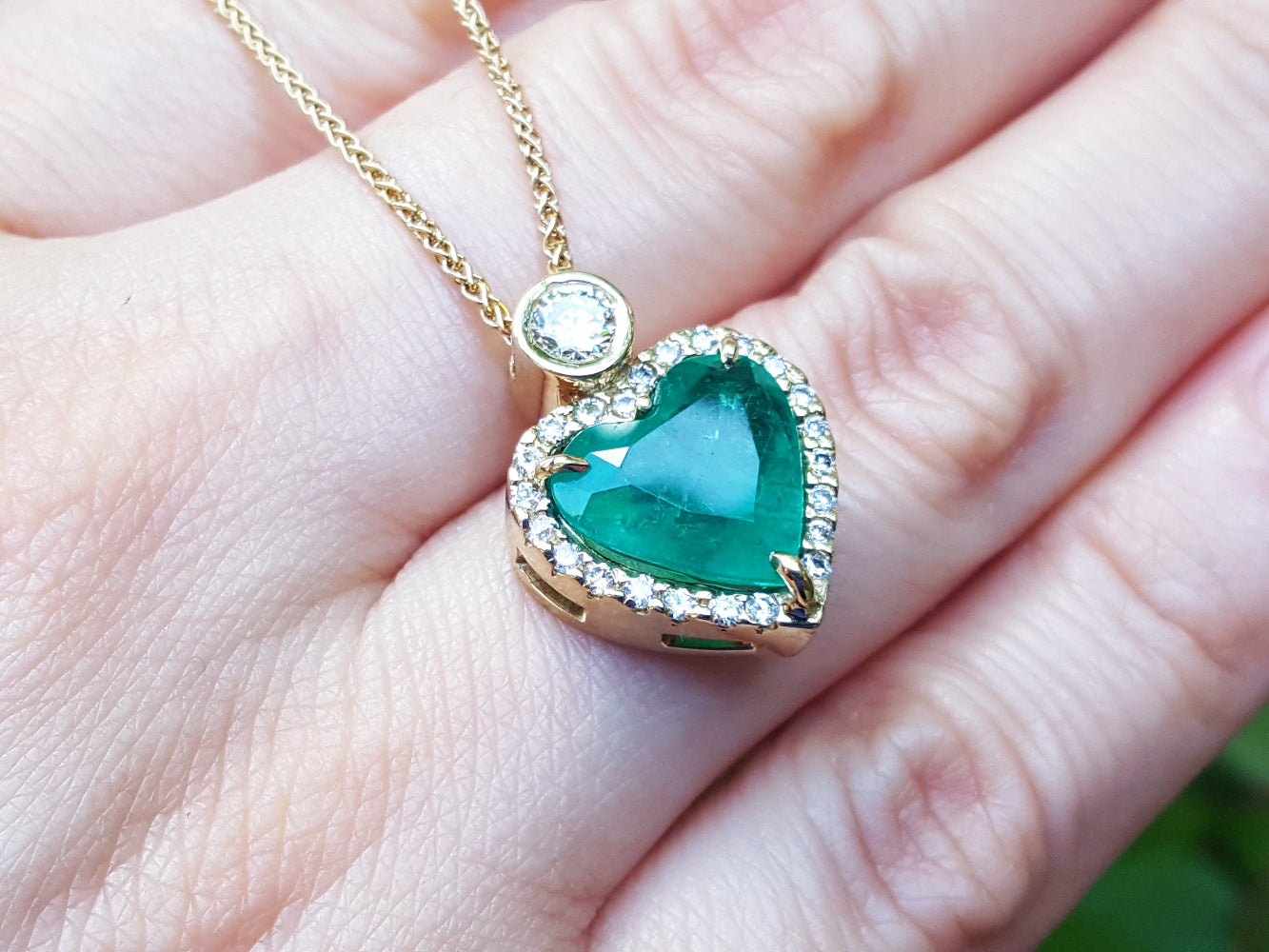 Heart-shaped emerald pendant with gold chain on a hand.