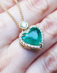 Heart-shaped emerald pendant with gold chain on a hand.
