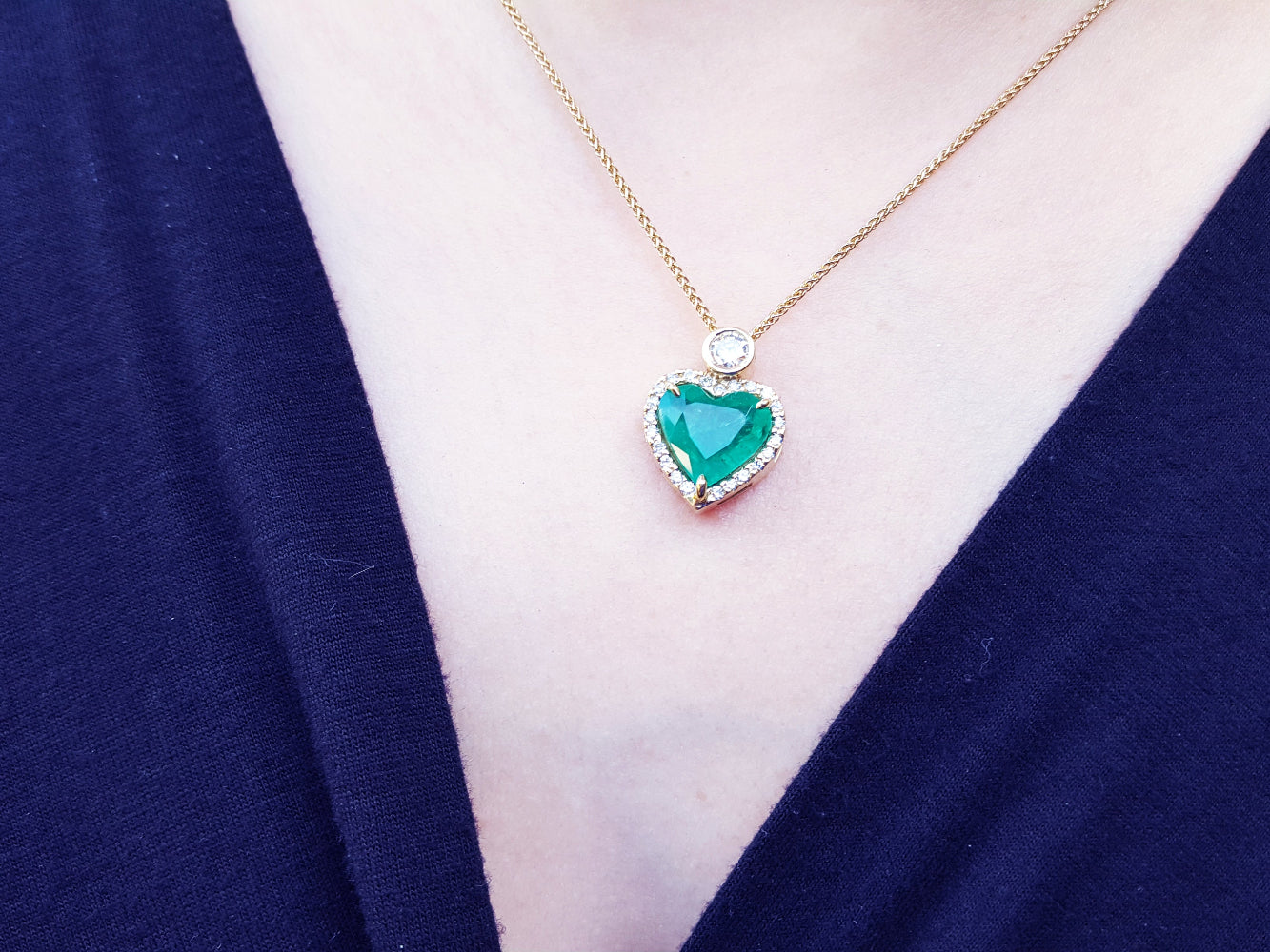 Heart-shaped emerald pendant necklace on a person chest with a blue garment.