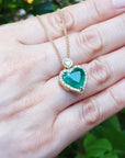 Hand holding a necklace with a emerald heart-shaped pendant against a blurred green background.