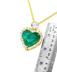 Heart-shaped emerald pendant with gold border and white diamond on top, next to a ruler for scale on a white background.