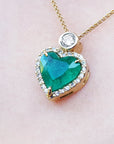 Heart-shaped emerald pendant with gold chain on a light pink background