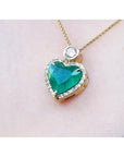 Heart-shaped emerald pendant with gold chain on a light pink background