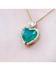 Heart-shaped emerald pendant with gold chain on a light pink background
