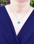 A woman wearing a blue blazer with a gold necklace featuring a natural emerald heart pendant.
