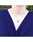 Heart-shaped emerald and diamond halo pendant in 18k gold, worn on a woman's neck.