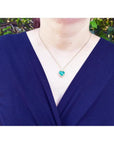 Heart-shaped emerald and diamond halo pendant in 18k gold, worn on a woman's neck.