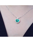 Natural emerald heart pendant in 14K white gold with diamond halo on a delicate chain, worn on a person.