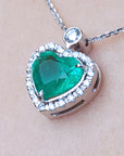 Heart-shaped emerald pendant with diamond accents on a beige skin background.