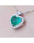 Heart-shaped emerald pendant with diamond accents on a beige skin background.