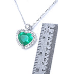 Heart-shaped emerald pendant on a chain with a ruler for scale on a white background.