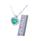 Heart-shaped emerald pendant on a chain with a ruler for scale on a white background.