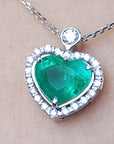 Heart-shaped emerald pendant with diamond accents on a silver chain topside view.