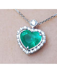 Heart-shaped emerald pendant with diamond accents on a silver chain topside view.