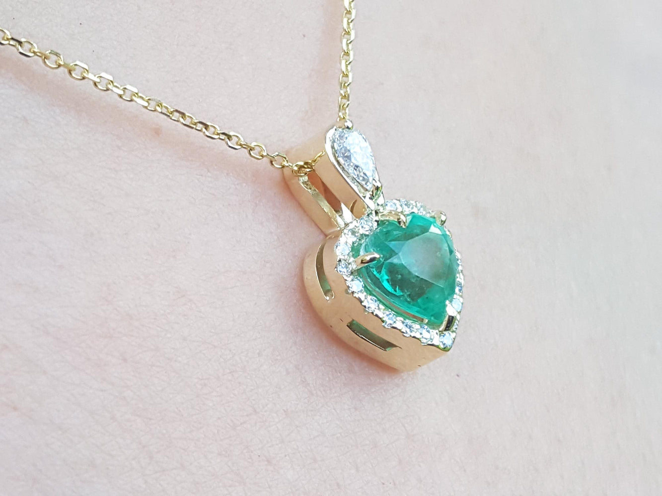 Gold necklace with a natural emerald pendant on a light pink background.
