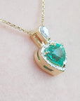 Gold necklace with a natural emerald pendant on a light pink background.