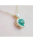 14K yellow gold heart pendant with a medium-deep green emerald and diamond halo on a delicate chain.