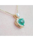 14K yellow gold heart pendant with a medium-deep green emerald and diamond halo on a delicate chain.