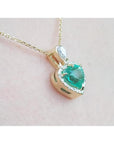 14K yellow gold heart pendant with a medium-deep green emerald and diamond halo on a delicate chain.