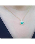 Heart-shaped emerald and diamond halo pendant in 14K yellow gold on a woman's neck.
