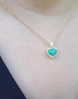 Gold necklace with a heart-shaped emerald pendant on a person wearing a dark top.