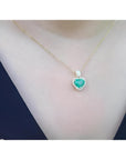 Heart-shaped emerald and diamond halo pendant in 14K yellow gold on a woman's neck.