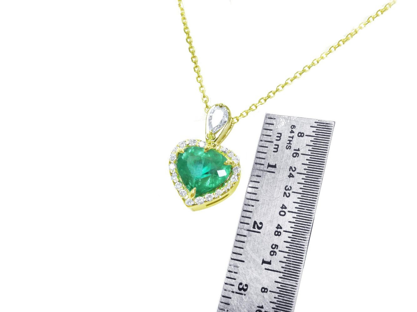 Gold necklace with a heart-shaped emerald pendant next to a ruler for size reference on a white background