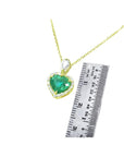 14K yellow gold heart pendant with a deep green emerald and diamond halo, next to a ruler.