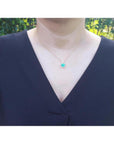 Heart-shaped emerald and diamond pendant in 14K yellow gold, worn on a woman's neck.