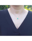 Heart-shaped emerald and diamond pendant in 14K yellow gold, worn on a woman's neck.