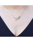 14K yellow gold twig necklace with a pear-cut natural emerald and diamond leaves on a woman's neck.