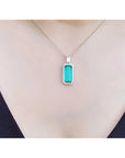 Elongated natural emerald pendant with halo diamonds on an 18K white gold chain, worn on a person.