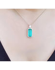 Elongated natural emerald pendant with halo diamonds on an 18K white gold chain, worn on a person.