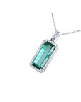 The topside view of a natural emerald pendant with halo diamond on a white background