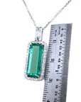 Genuine Colombian emerald pendant with white gold chain with a ruler for scale on a white background
