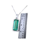 Elongated natural emerald pendant with halo diamonds in 18K white gold, shown next to a ruler.