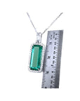 Elongated natural emerald pendant with halo diamonds in 18K white gold, shown next to a ruler.